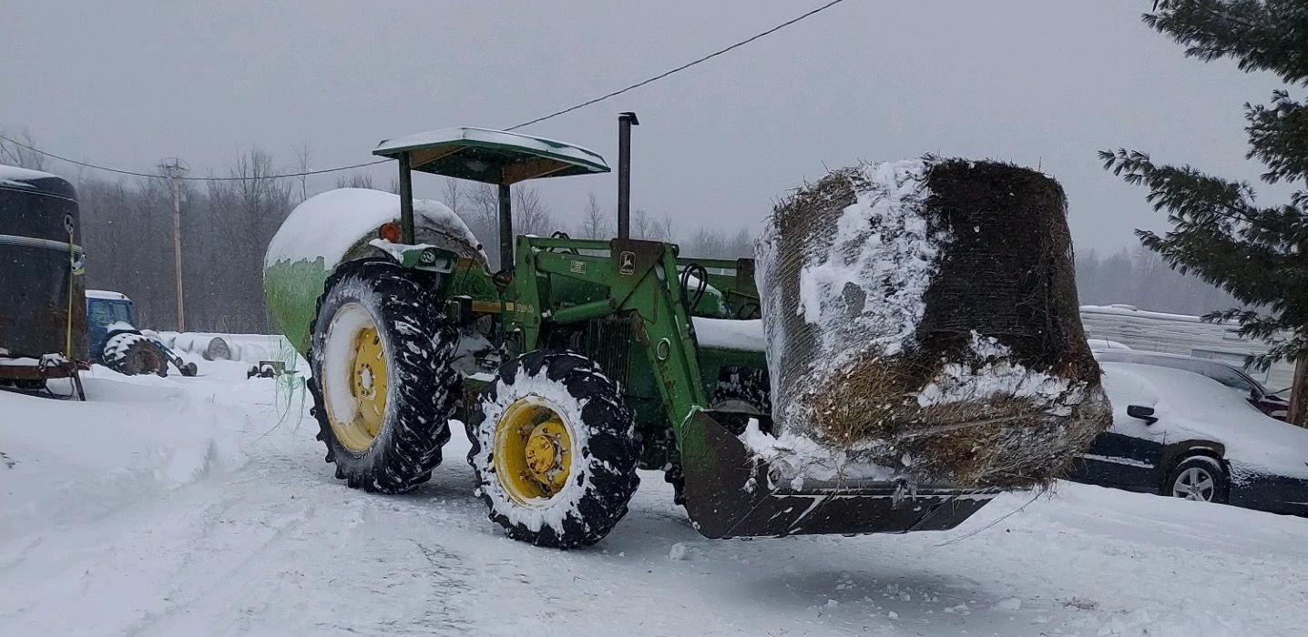 John Deere tractor carrying a hay bale in the snow