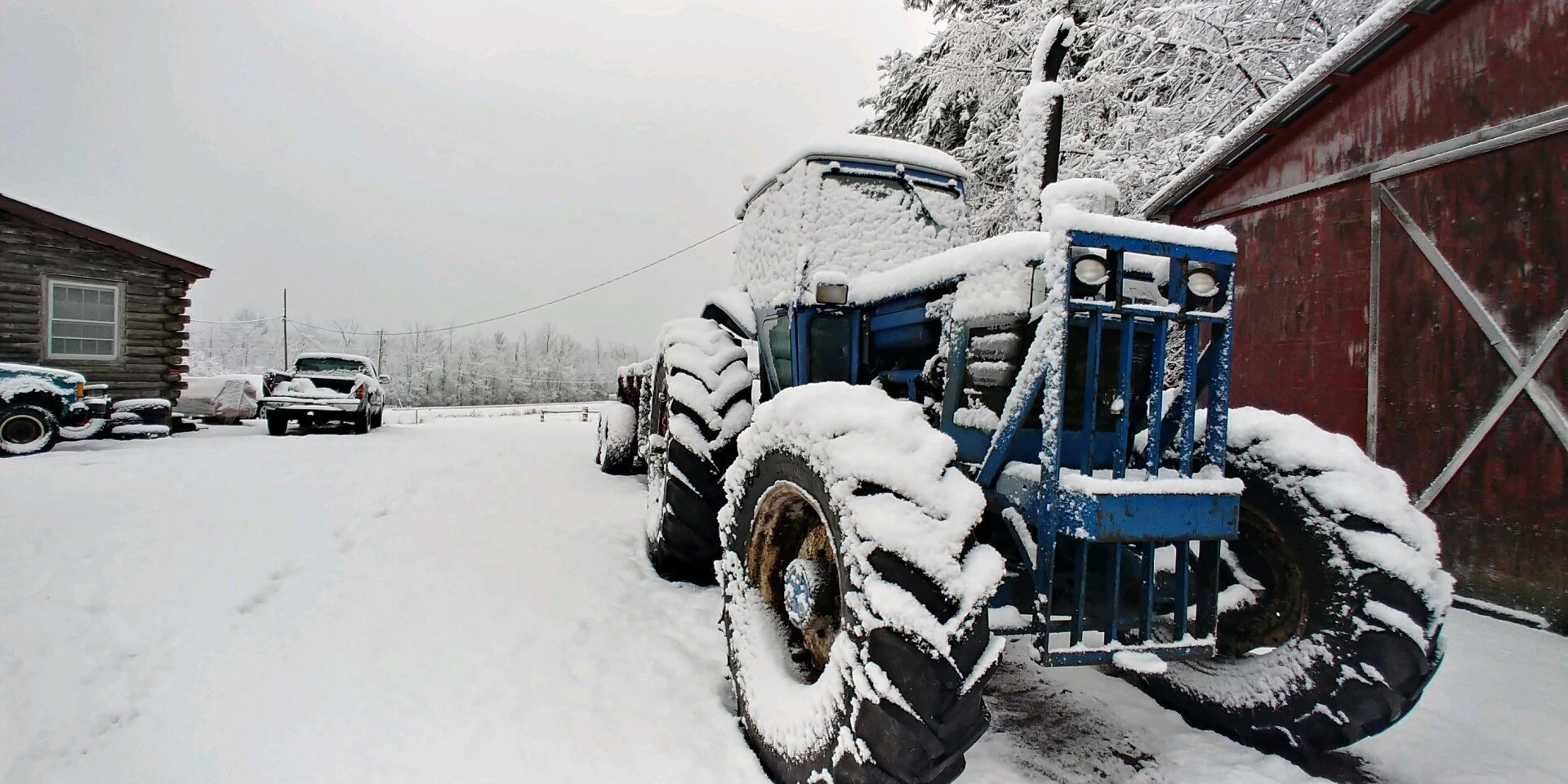 Blue tractor covered in snow by the barn